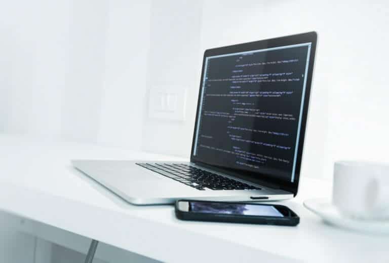 Web Application Developer Desk with Modern Laptop Computer and Website Source Code on Display. Mobile Work Concept.